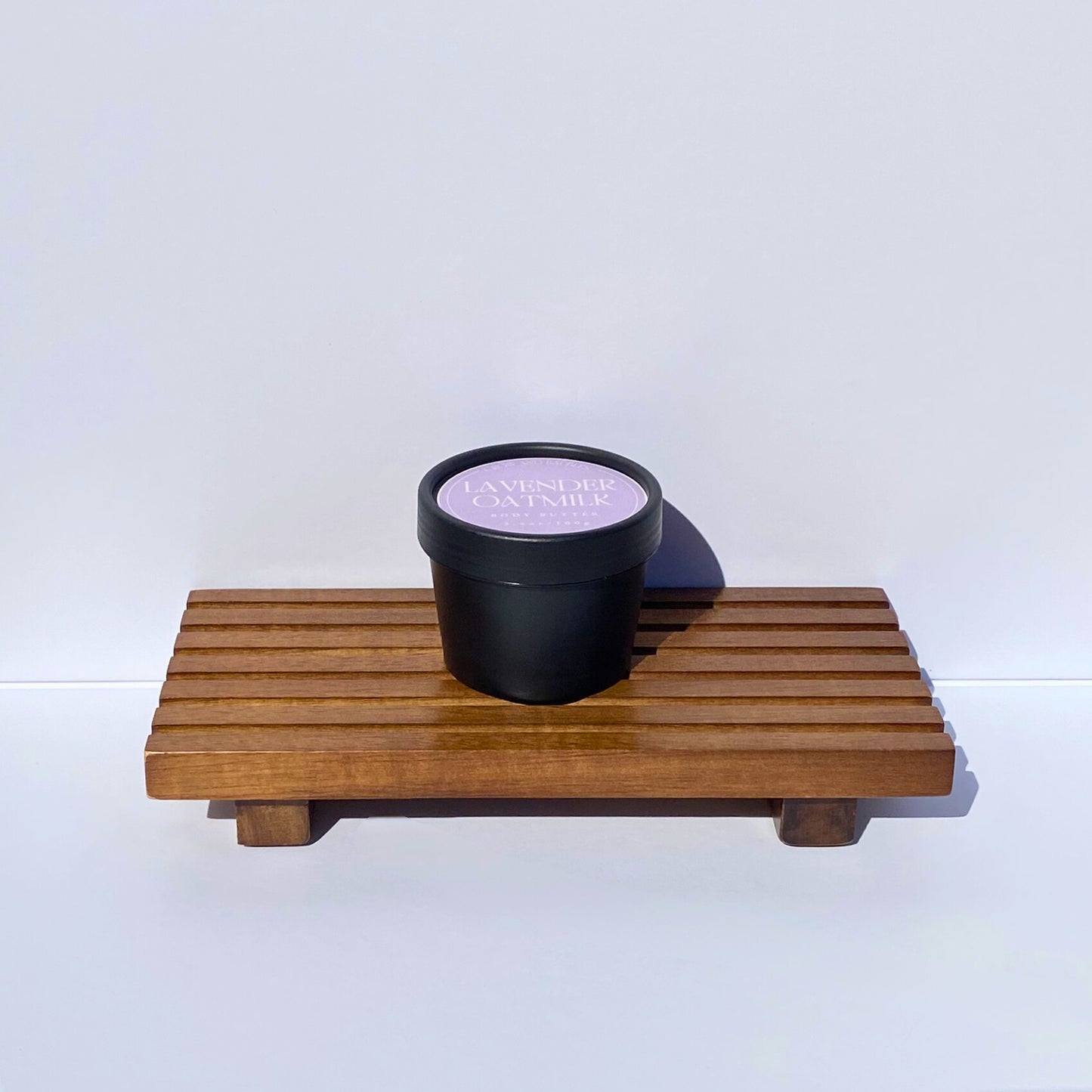 Black container with lavender label on a wooden tray against a white background