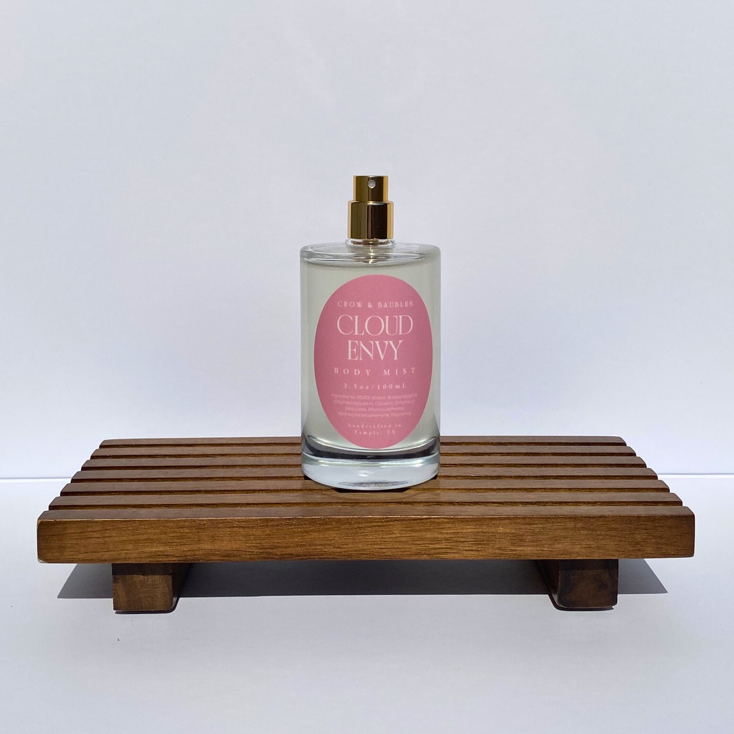 Glass spray bottle labeled 'Clued Envy' on a wooden stand with a white background