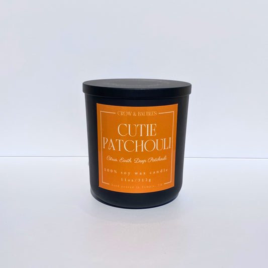 Black candle with an orange label "cutie patchouli" on a white background
