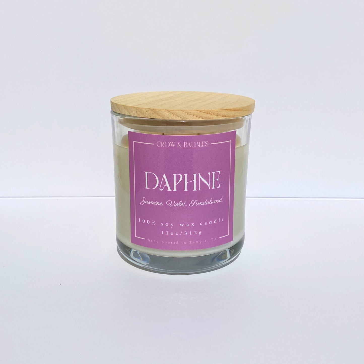 Glass candle with a pink label "Daphne" on a white background