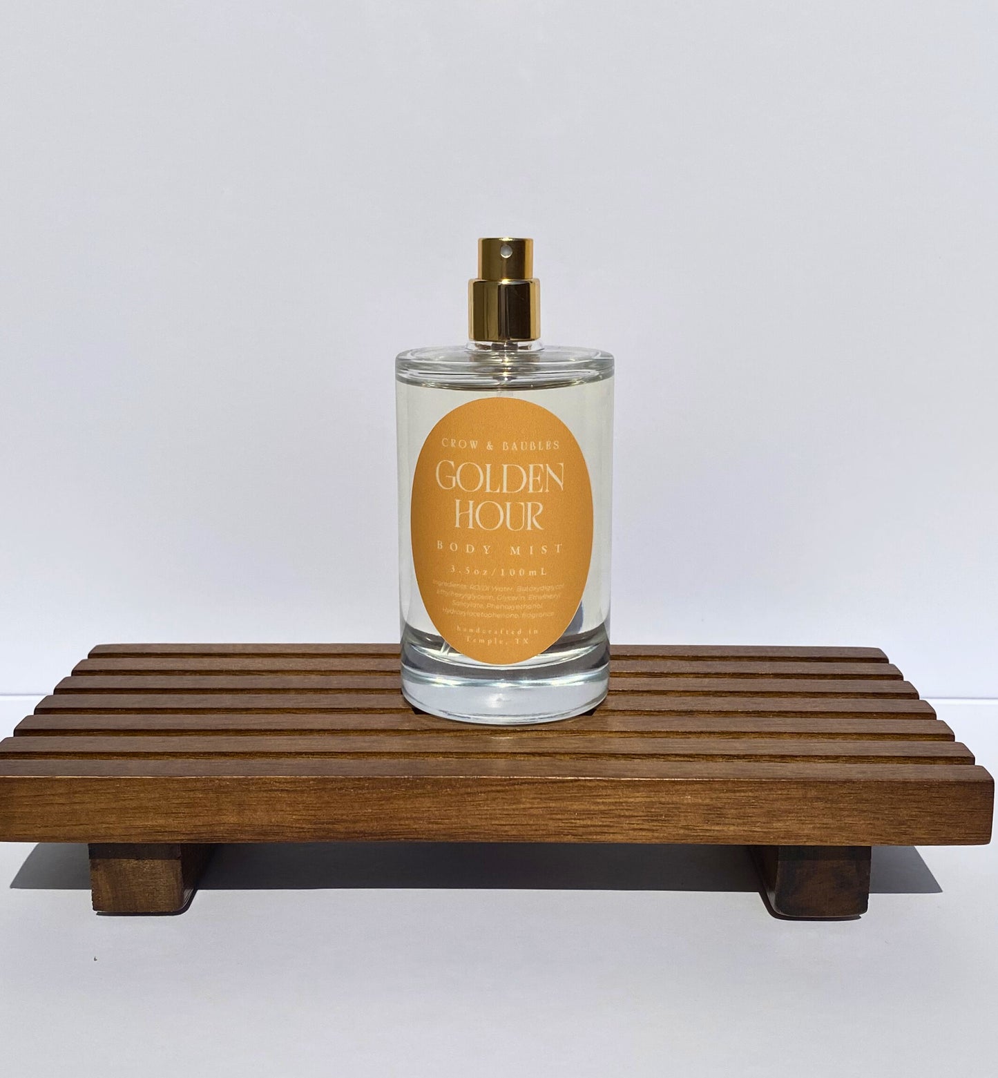 Perfume bottle labeled 'Golden Hour' on a wooden stand with a white background