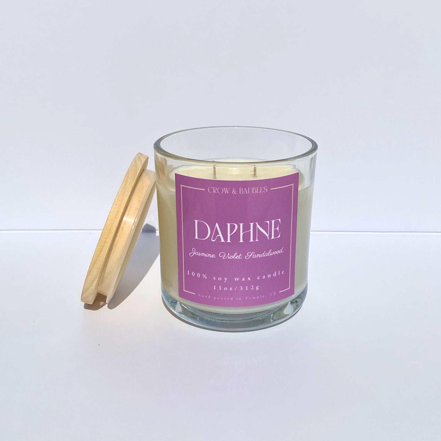 Glass candle with a pink label "Daphne" on a white background