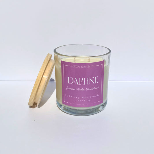 Glass candle with a pink label "Daphne" on a white background