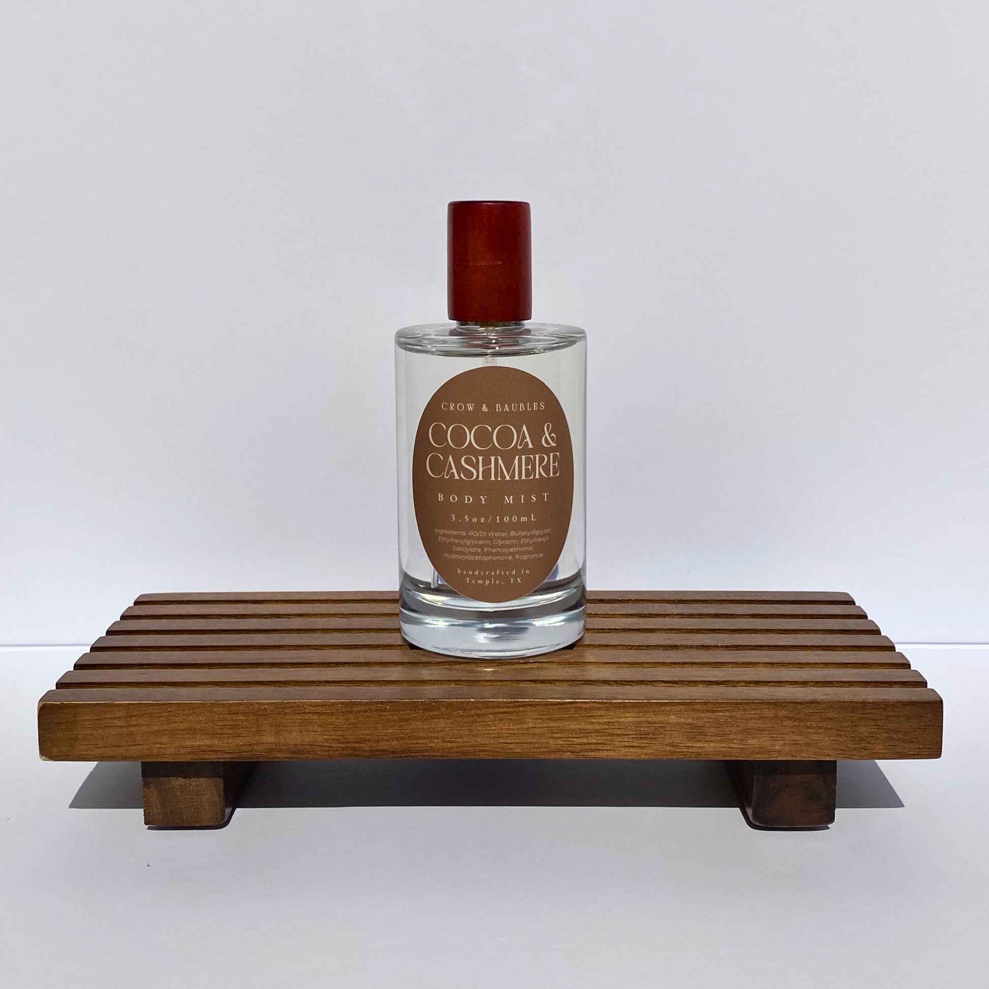 Bottle of 'Cocoa & Cashmere' body mist on a wooden stand with a white background