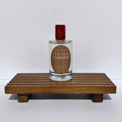 Bottle of 'Cocoa & Cashmere' body mist on a wooden stand with a white background