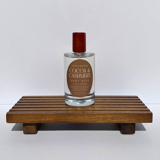 Bottle of 'Cocoa & Cashmere' body mist on a wooden stand with a white background