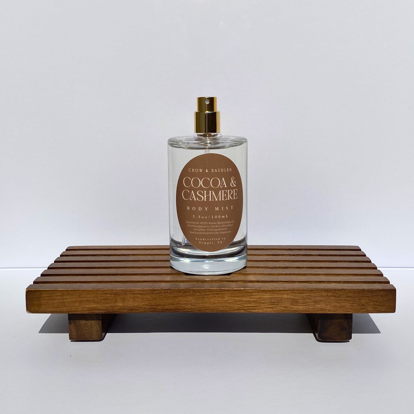 Bottle of 'Cocoa & Cashmere' body mist on a wooden stand with a white background