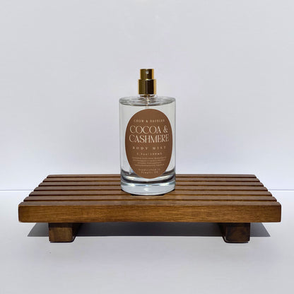 Bottle of 'Cocoa & Cashmere' body mist on a wooden stand with a white background