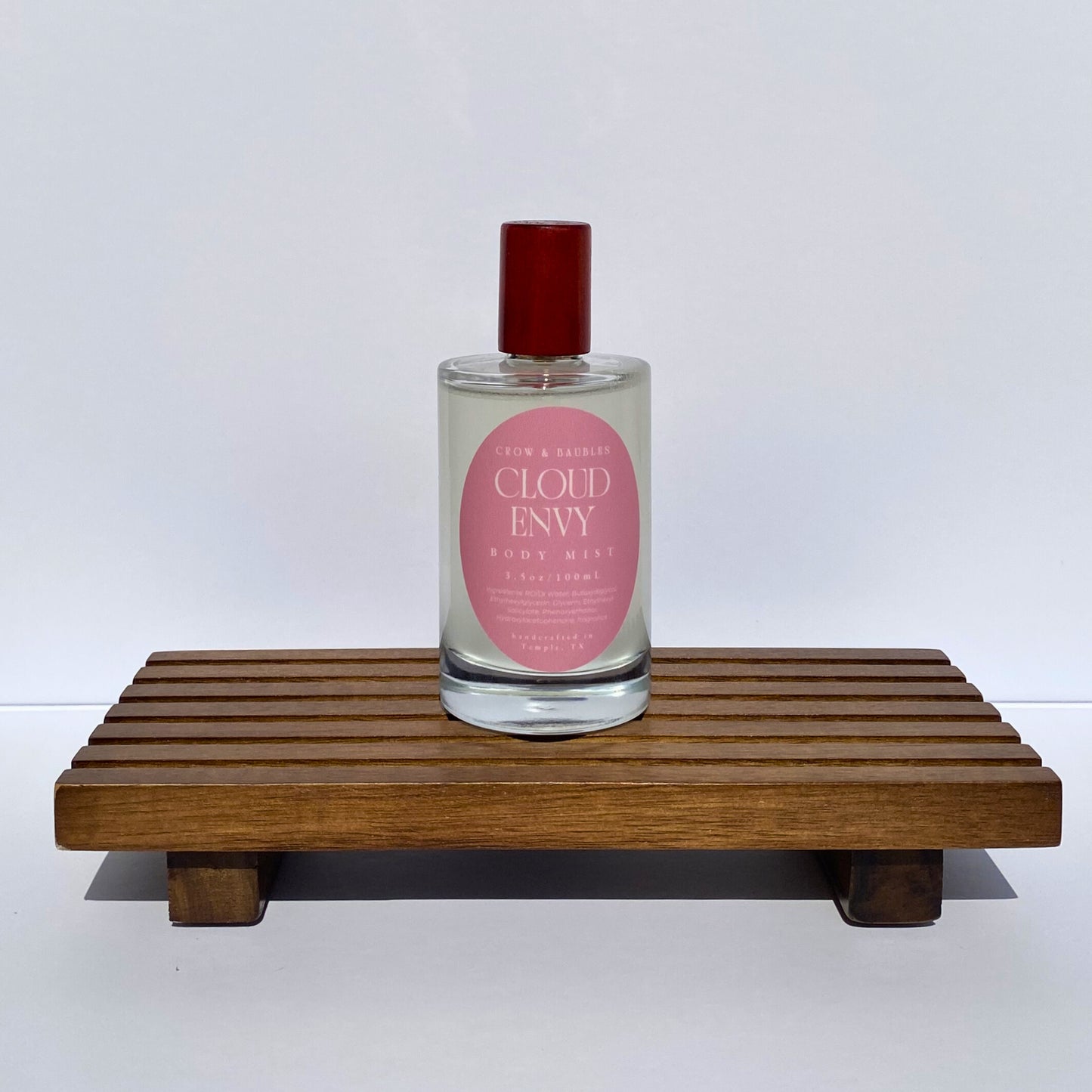 Bottle of 'Cloud Envy' body mist on a wooden stand with a white background