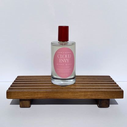 Bottle of 'Cloud Envy' body mist on a wooden stand with a white background