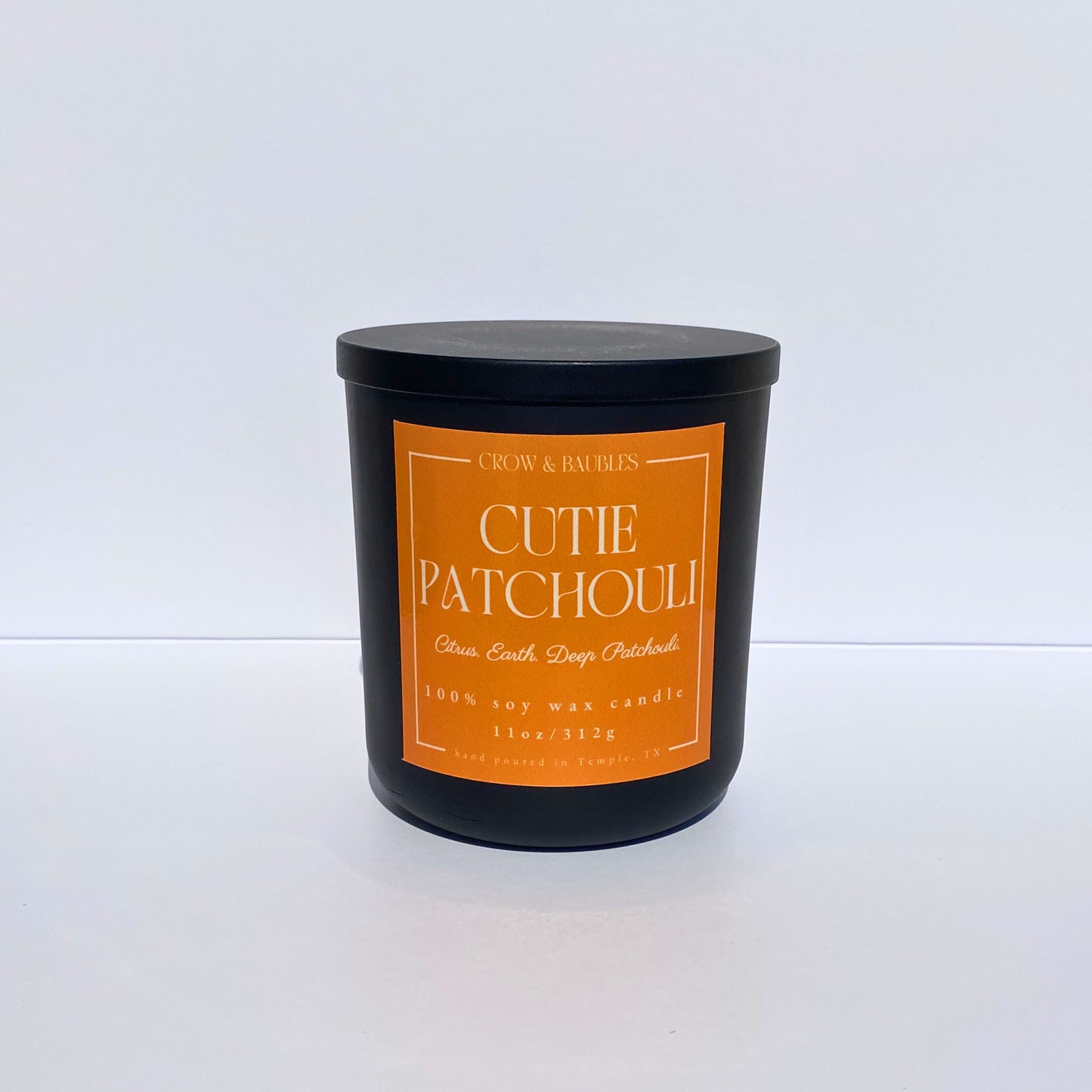 Black candle with an orange label "cutie patchouli" on a white background 
