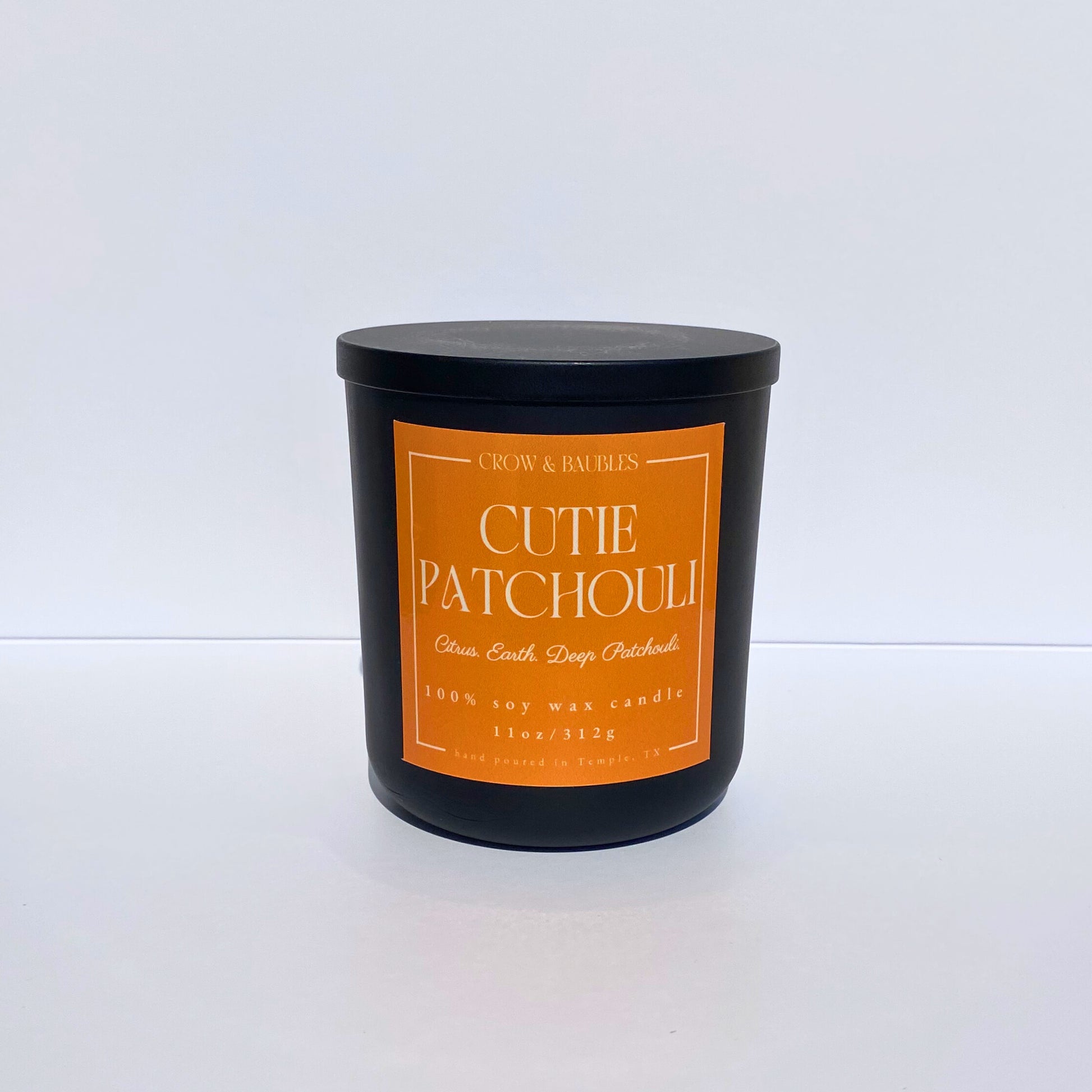 Black candle with an orange label "cutie patchouli" on a white background 