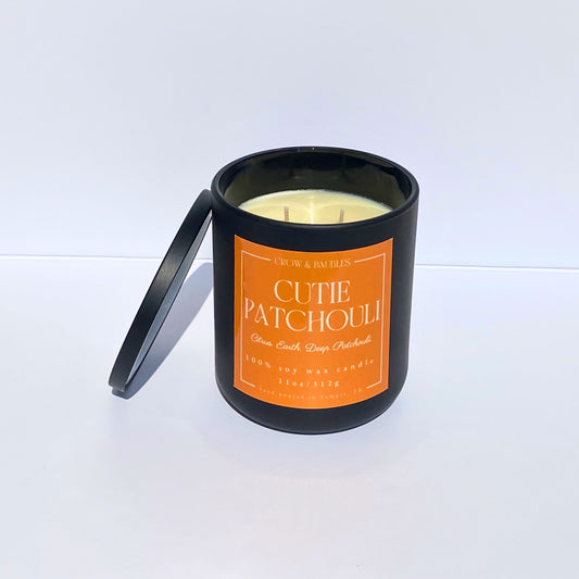 Candle in a black container with an orange label "Cutie Patchouli" on a white background