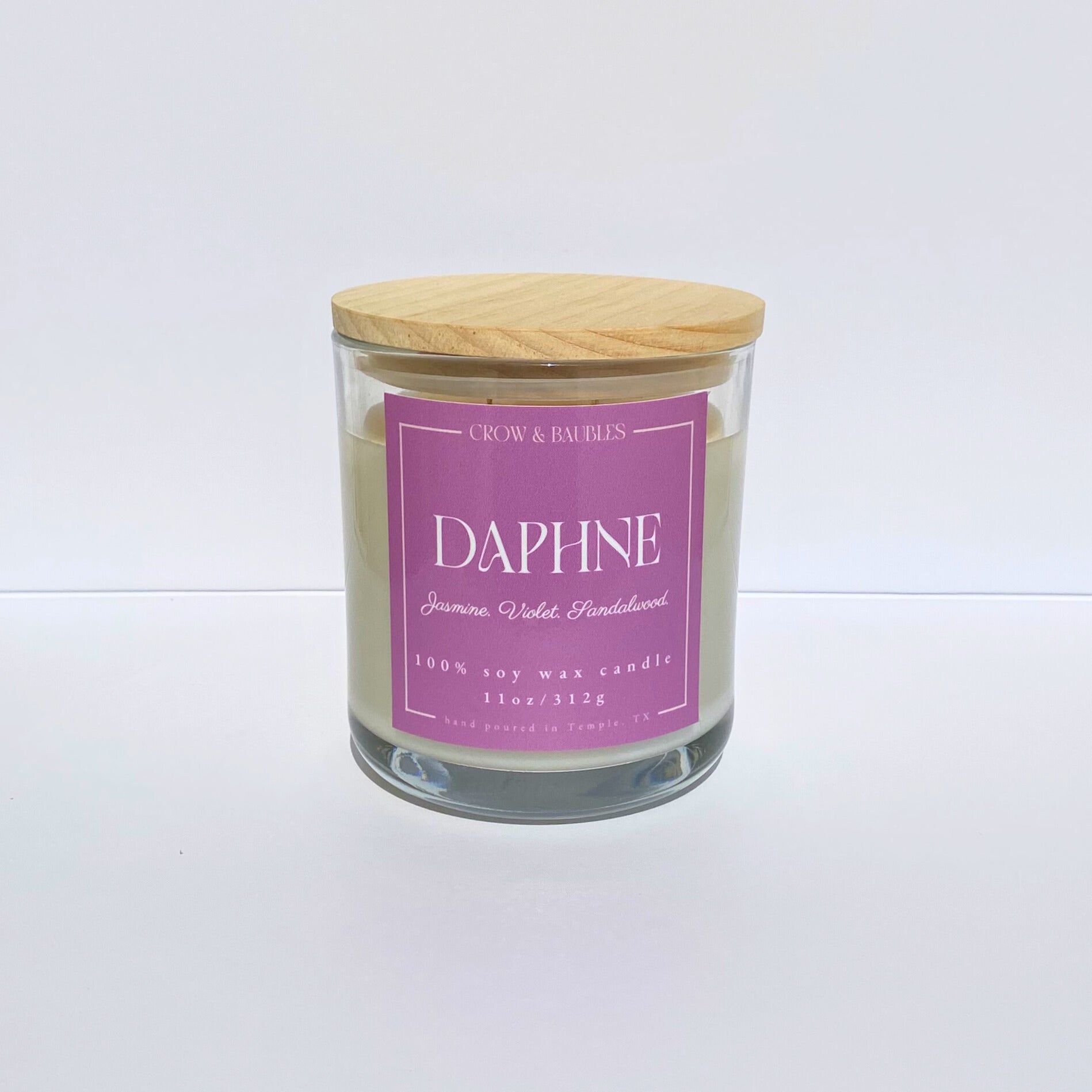 Glass candle with a pink label "Daphne" on a white background