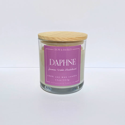 Glass candle with a pink label "Daphne" on a white background