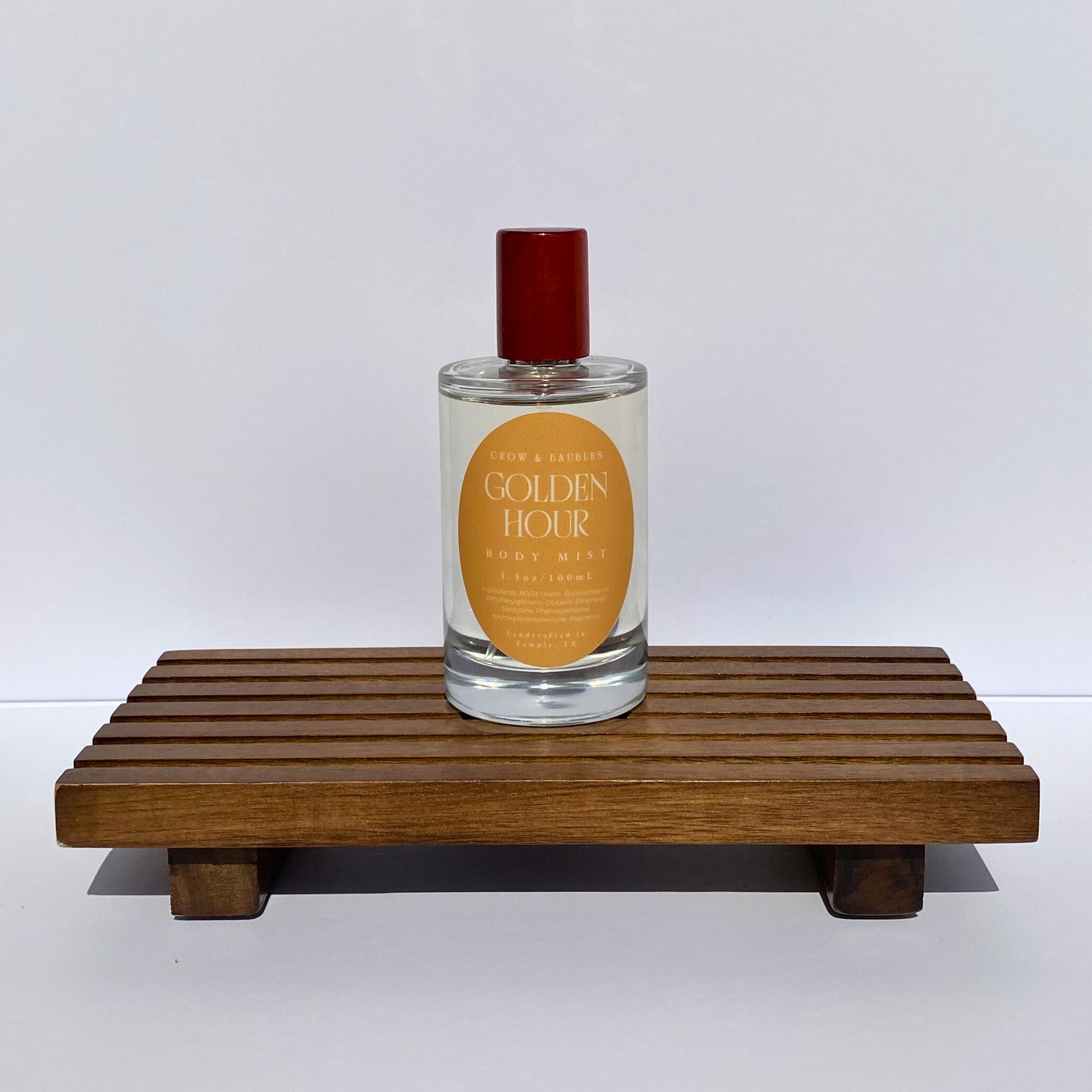 Perfume bottle labeled 'Golden Hour' on a wooden stand with a white background