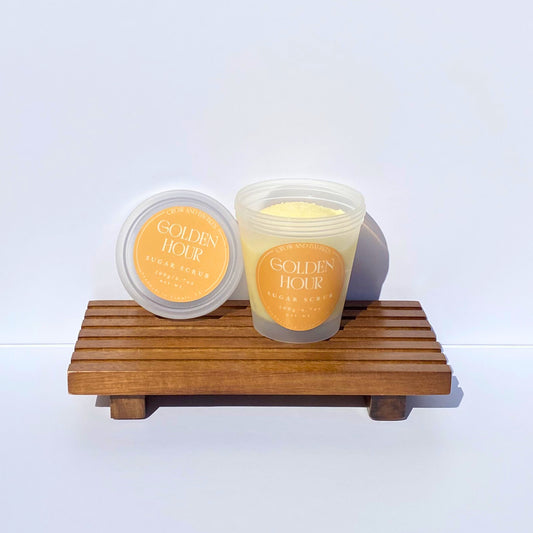 Clear sugar scrub container labeled 'Golden Hour' on a wooden stand with a white background 