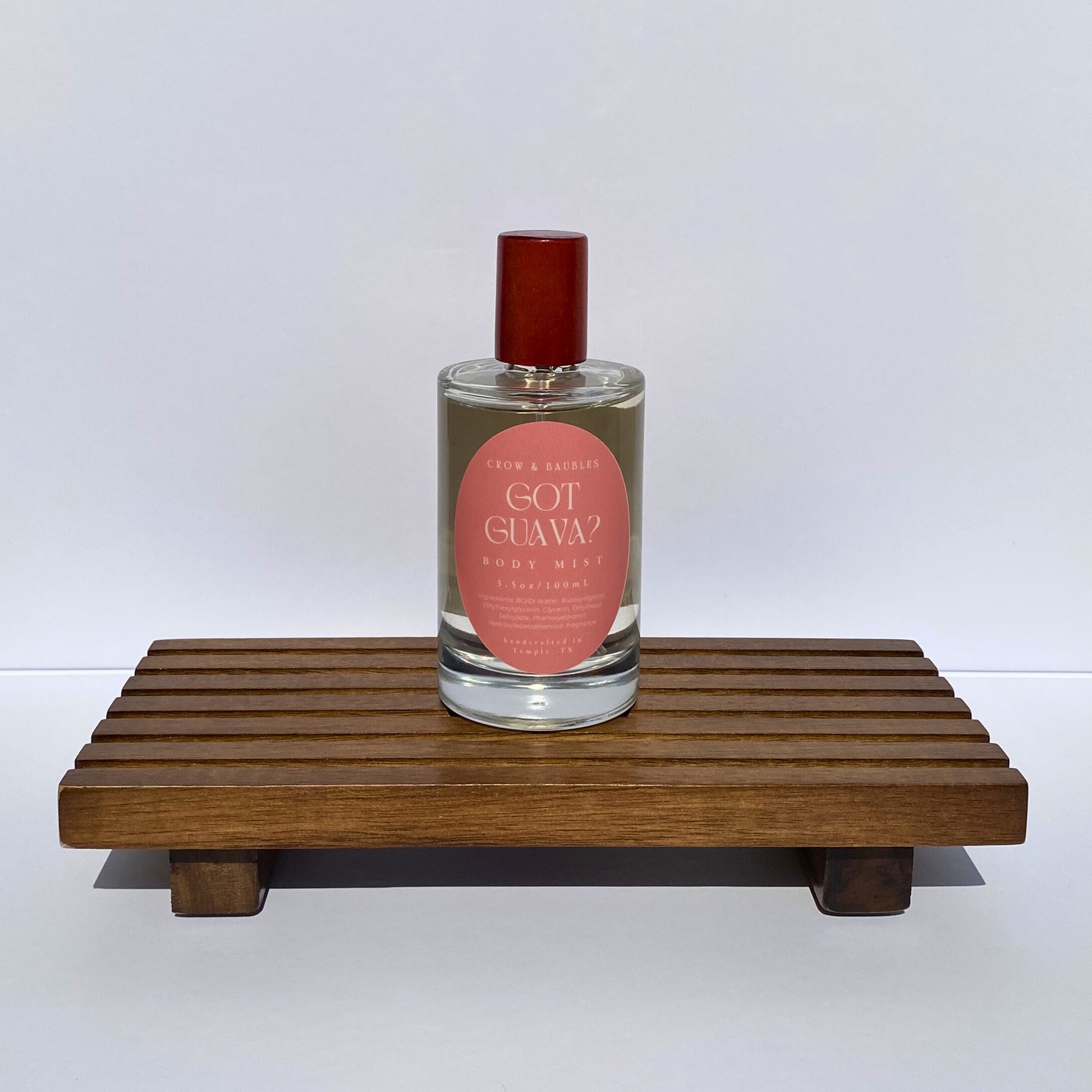 Bottle of 'Got Guava?' body mist on a wooden stand with a white background