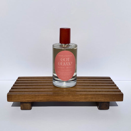 Bottle of 'Got Guava?' body mist on a wooden stand with a white background