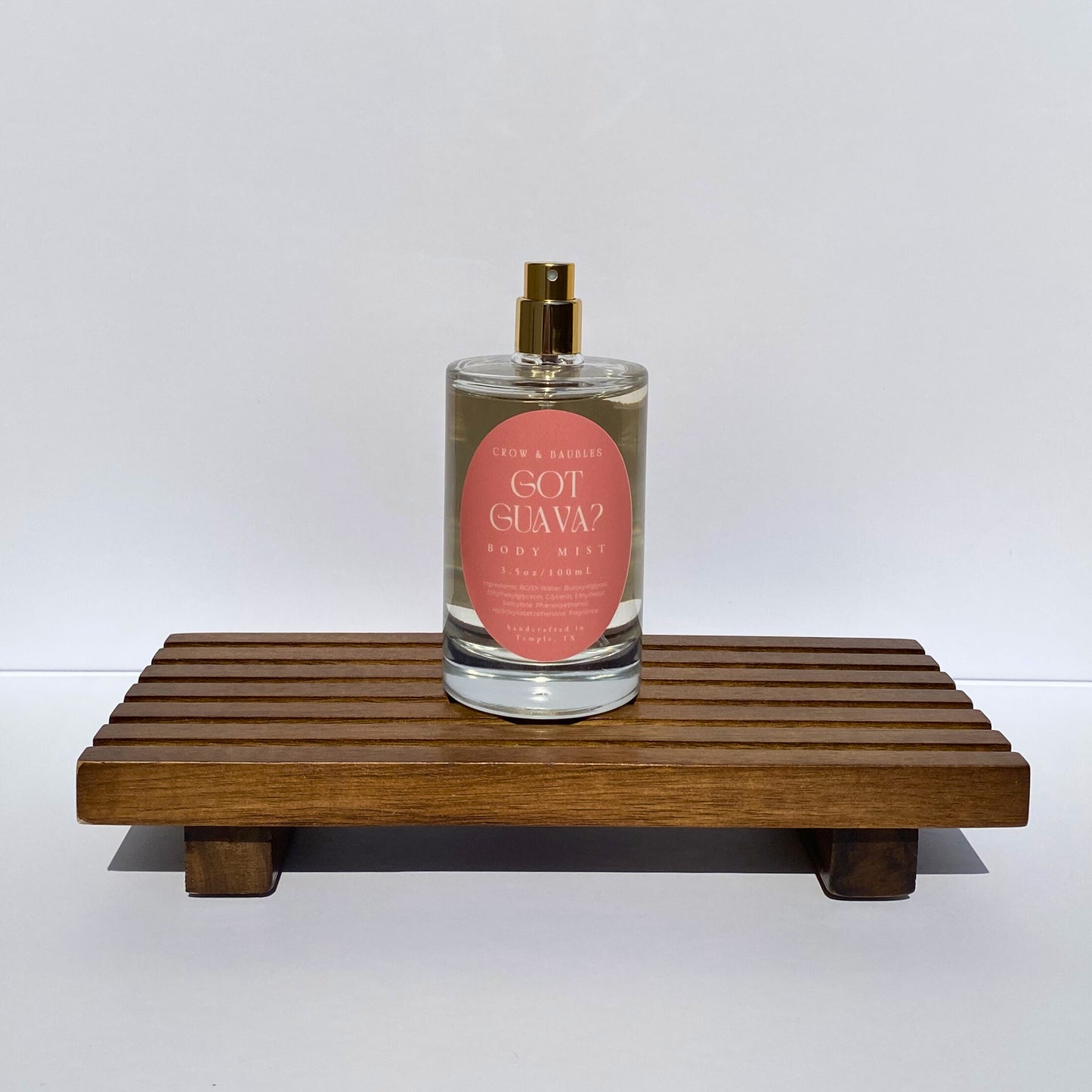 Perfume bottle labeled 'Got Guava?' on a wooden stand with a white background