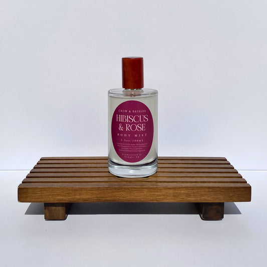 Bottle of 'Hibiscus & Rose' body mist on a wooden stand with a white background