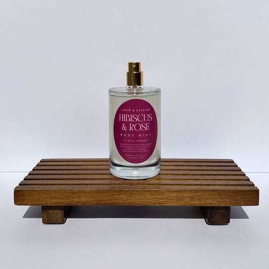 Body mist bottle labeled 'Hibiscus & Rose' on a wooden stand with a white background