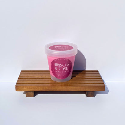 Pink jar of 'Hibiscus & Rose' sugar scrub on a wooden stand with a white background