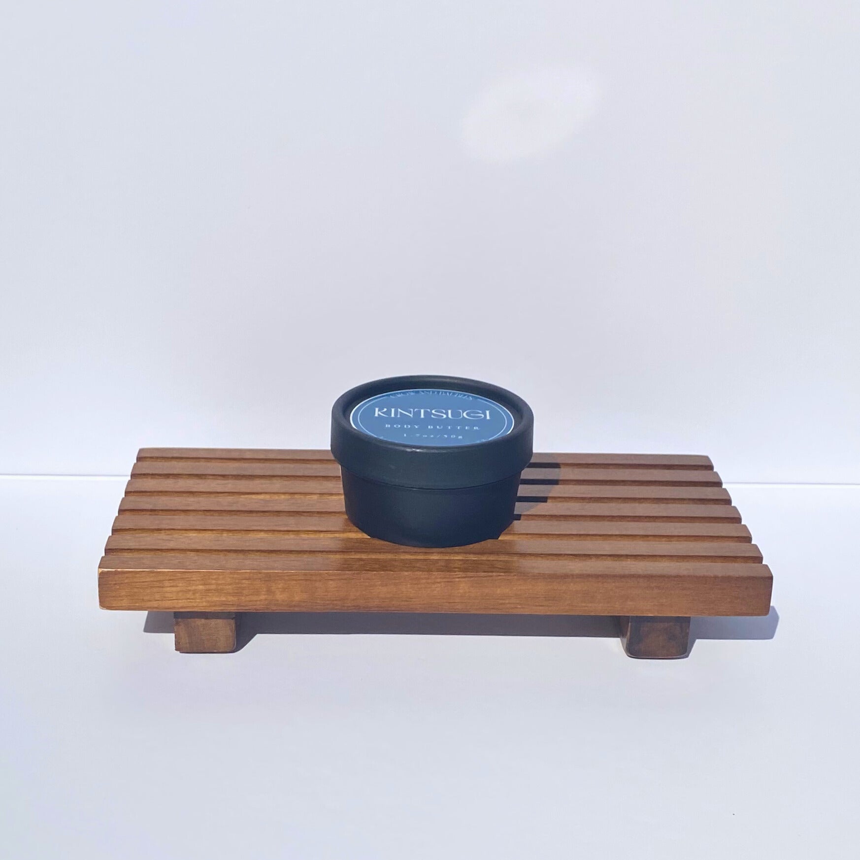 Black container with 'Kintsugi' branding on a wooden tray against a white background