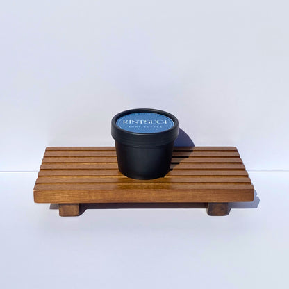 Black container with blue Kintsugi label on a wooden tray against a white background