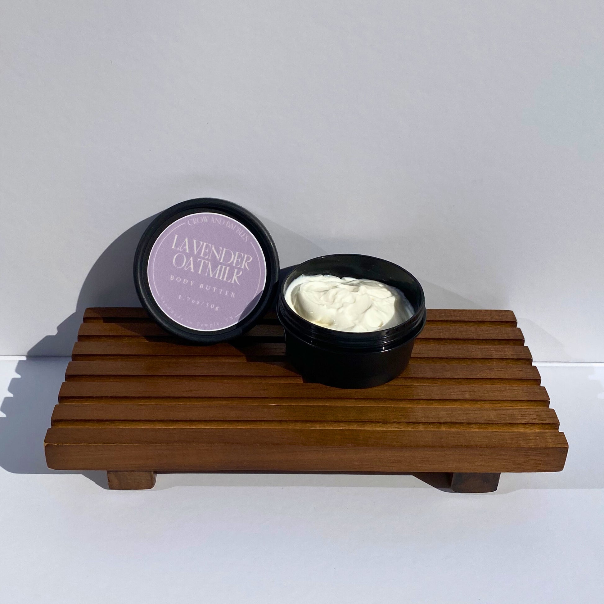 an open container of lavender oatmeal body butter on a wooden stand against a white background