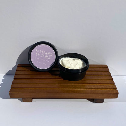 an open container of lavender oatmeal body butter on a wooden stand against a white background