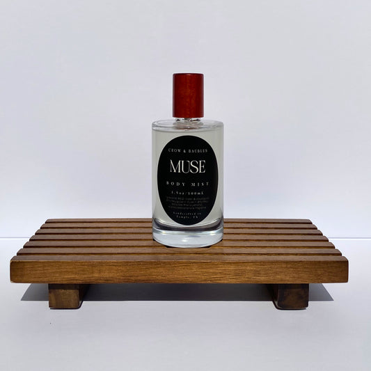 Bottle of 'Muse' body mist on a wooden stand with a white background