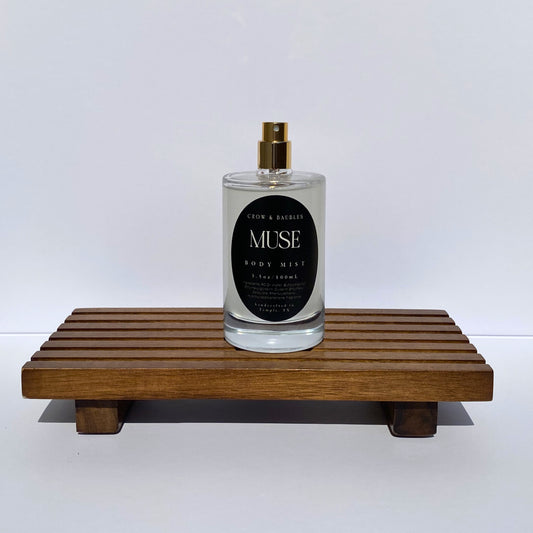Bottle of 'Muse' body mist on a wooden stand with a white background