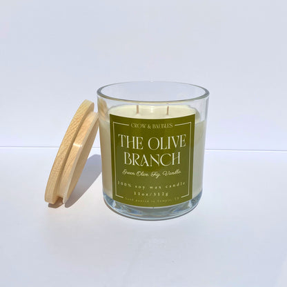 Candle labeled 'The Olive Branch' with a wooden lid on a white background